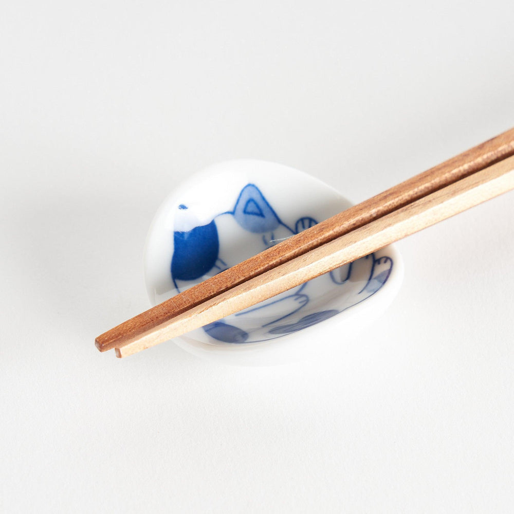 A small chopstick rest with a blue and white cat, playfully stretching one paw upwards.