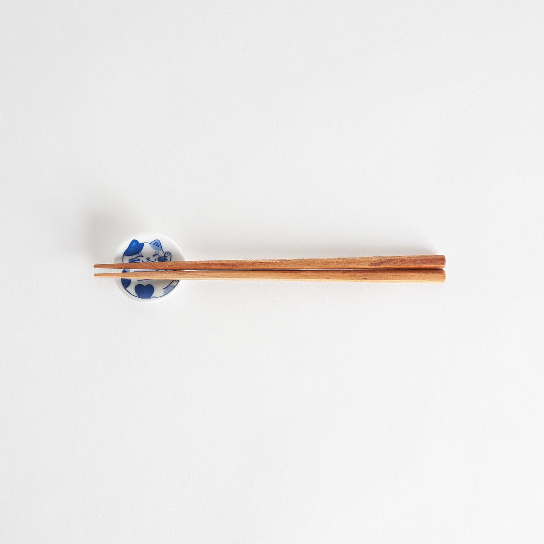 A small chopstick rest with a blue and white cat, playfully stretching one paw upwards.