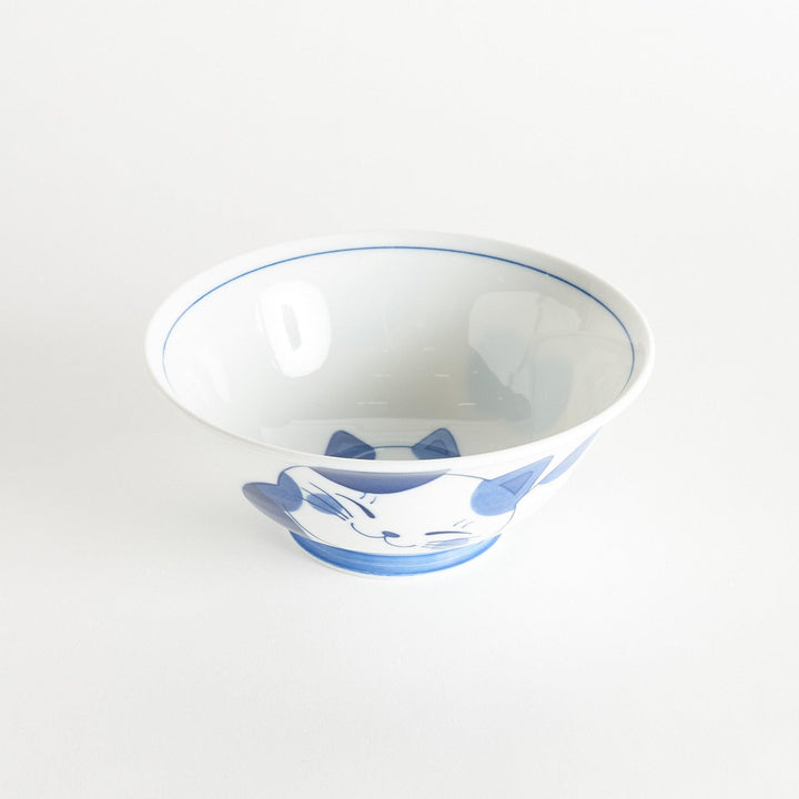 A white ramen bowl with a blue design of a cat with its ears back, looking relaxed.