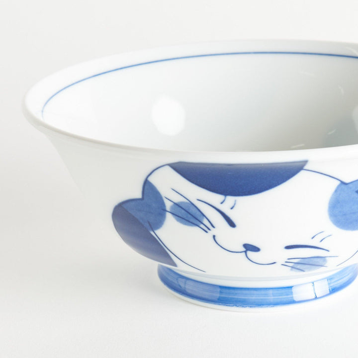 A white ramen bowl with a blue design of a cat with its ears back, looking relaxed.