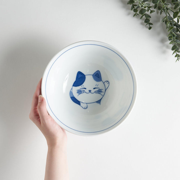 A white ramen bowl with a blue design of a cat with its ears back, looking relaxed.