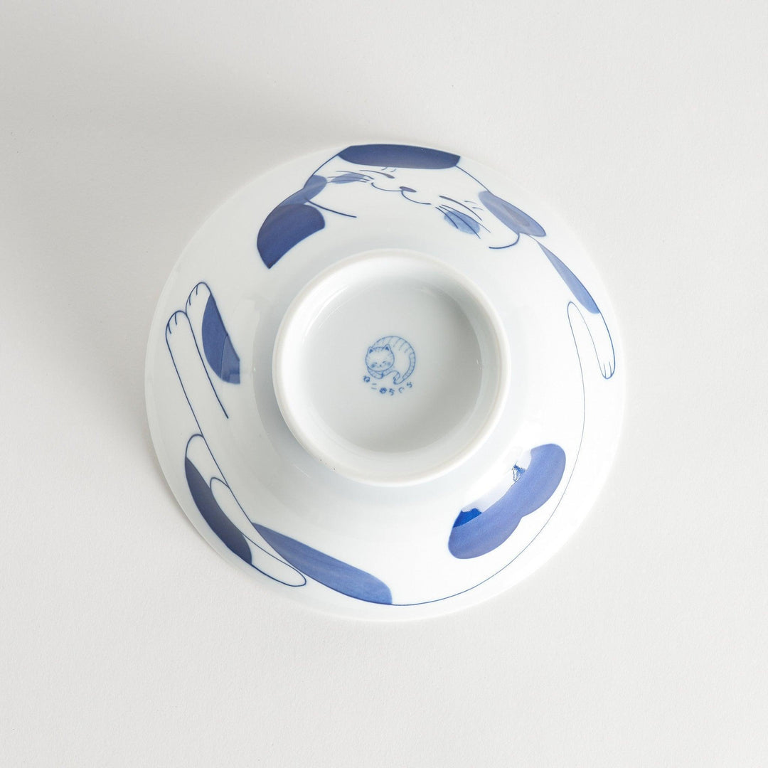 A white ramen bowl with a blue design of a cat with its ears back, looking relaxed.