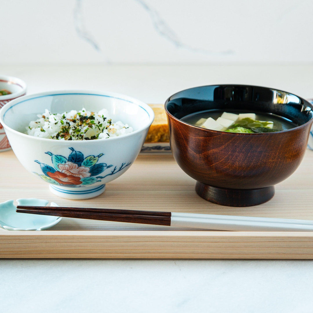 A small, white ceramic rice bowl with a colorful floral design in red, blue, and green.