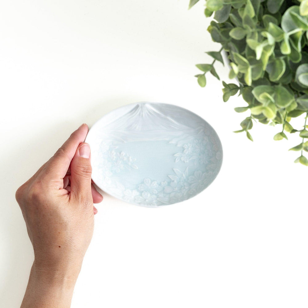 A round celadon dessert plate with a subtle raised pattern depicting Mount Fuji and surrounding nature, with a smooth, glossy finish.