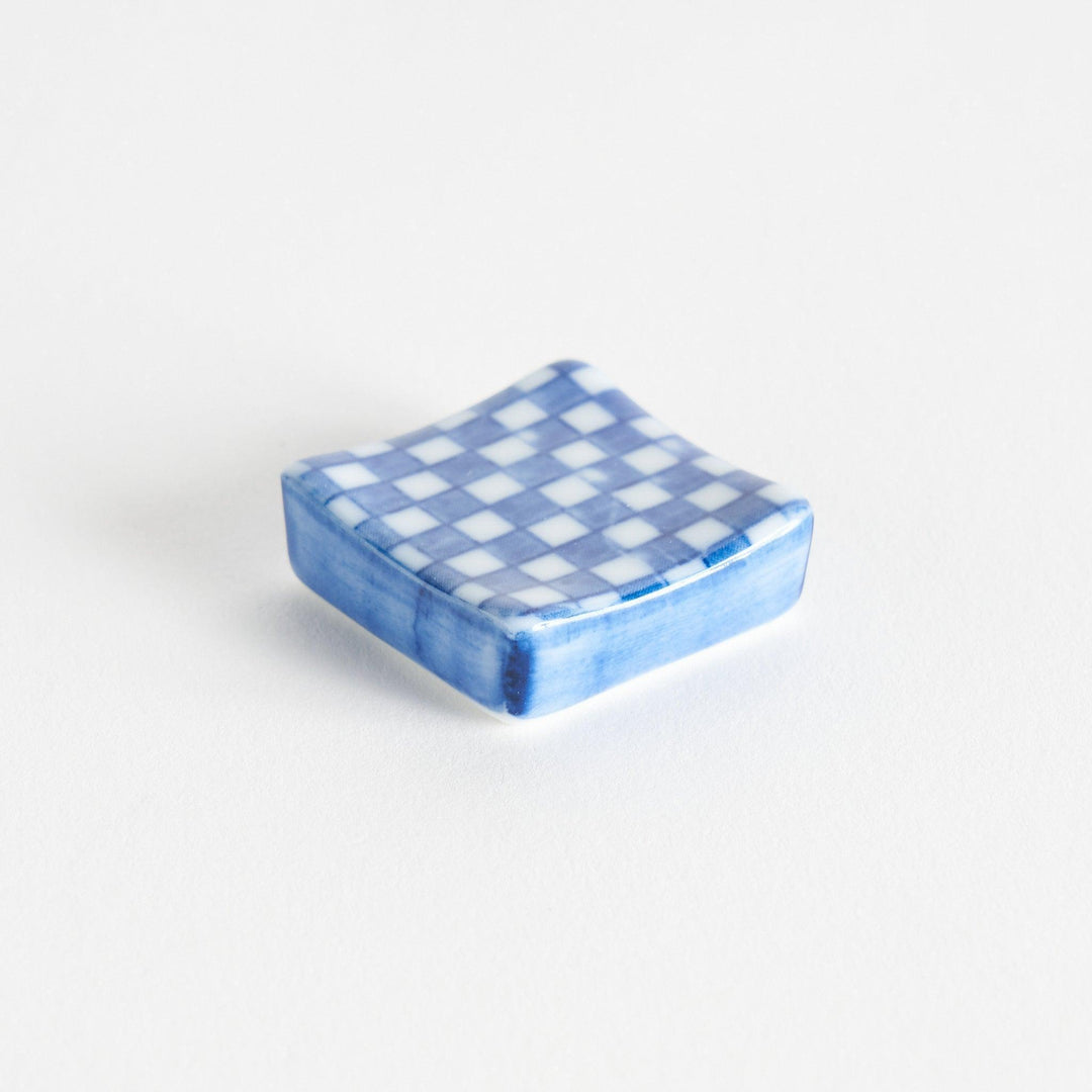 A blue and white checkered square-shaped ceramic chopstick rest.