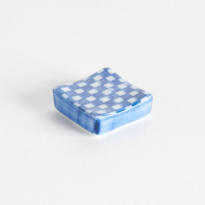 A blue and white checkered square-shaped ceramic chopstick rest.