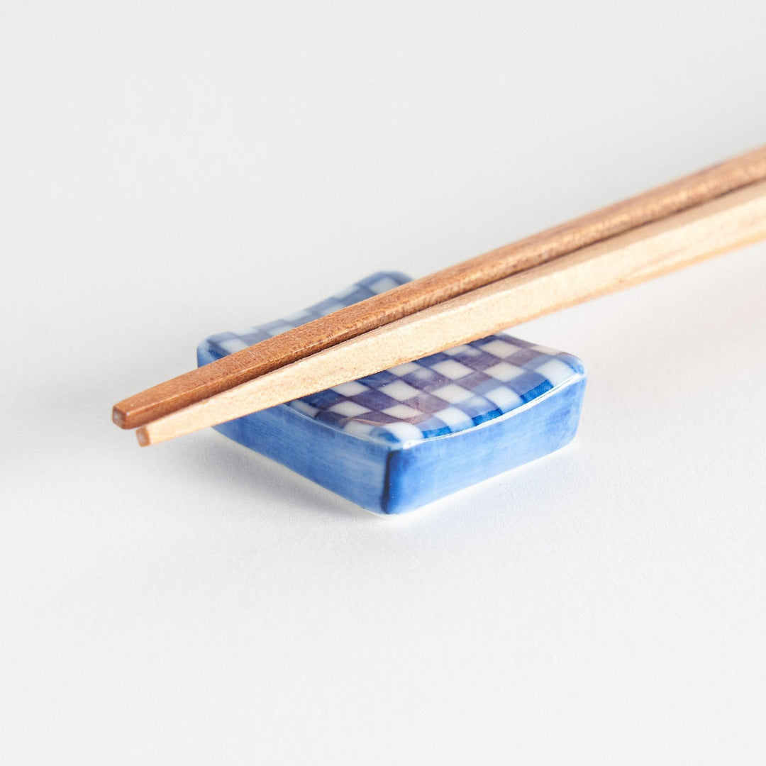 A blue and white checkered square-shaped ceramic chopstick rest.