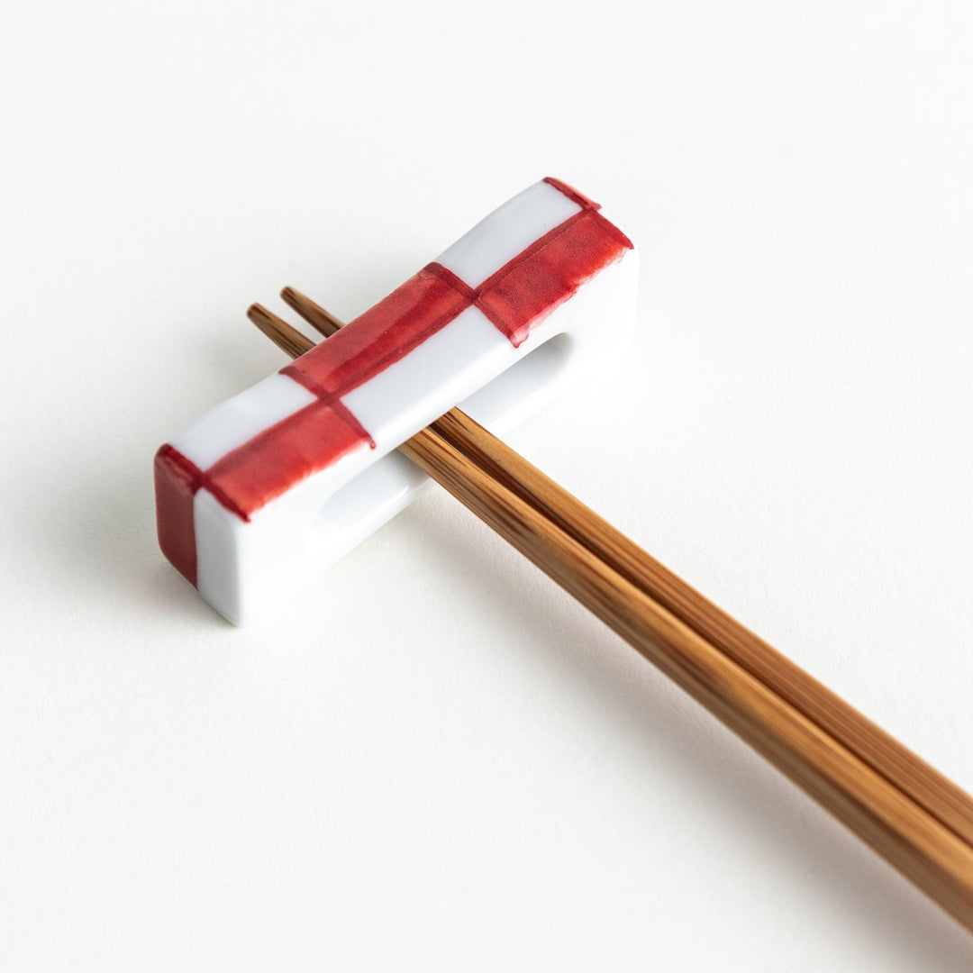 A small rectangular chopsticks rest, white with blue or red stripes arranged in a checkered pattern.