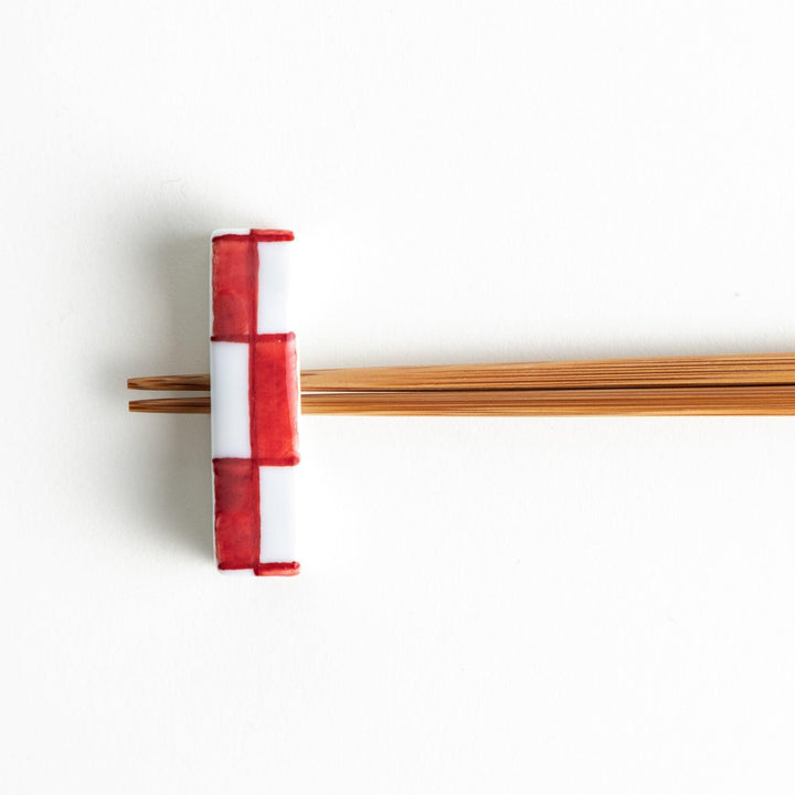 A small rectangular chopsticks rest, white with blue or red stripes arranged in a checkered pattern.