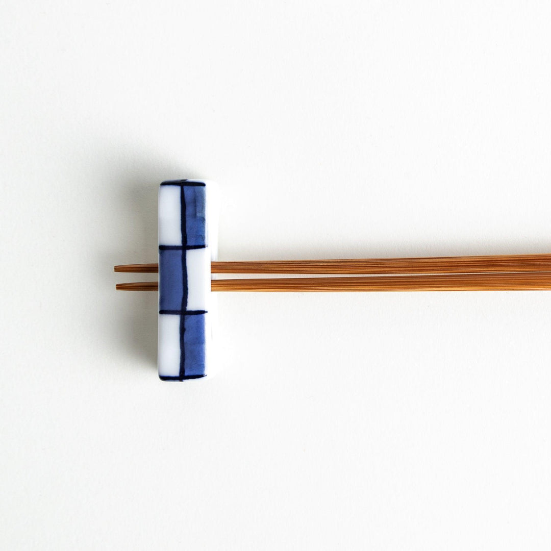 A small rectangular chopsticks rest, white with blue or red stripes arranged in a checkered pattern.