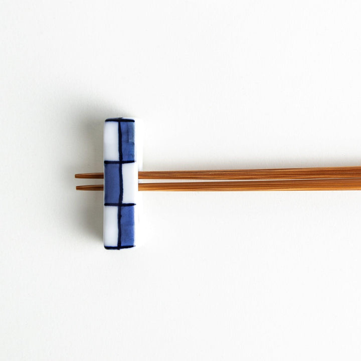 A small rectangular chopsticks rest, white with blue or red stripes arranged in a checkered pattern.