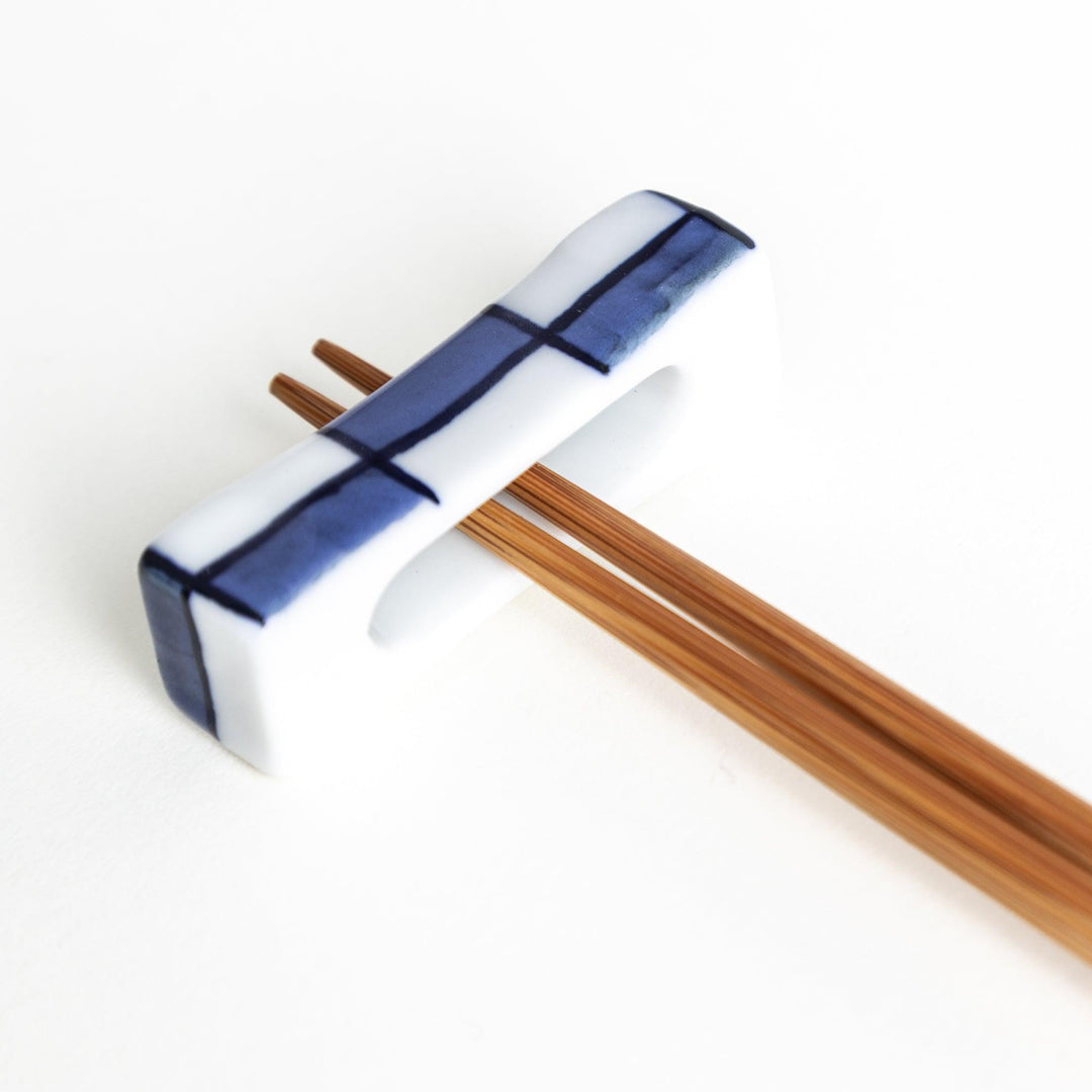 A small rectangular chopsticks rest, white with blue or red stripes arranged in a checkered pattern.