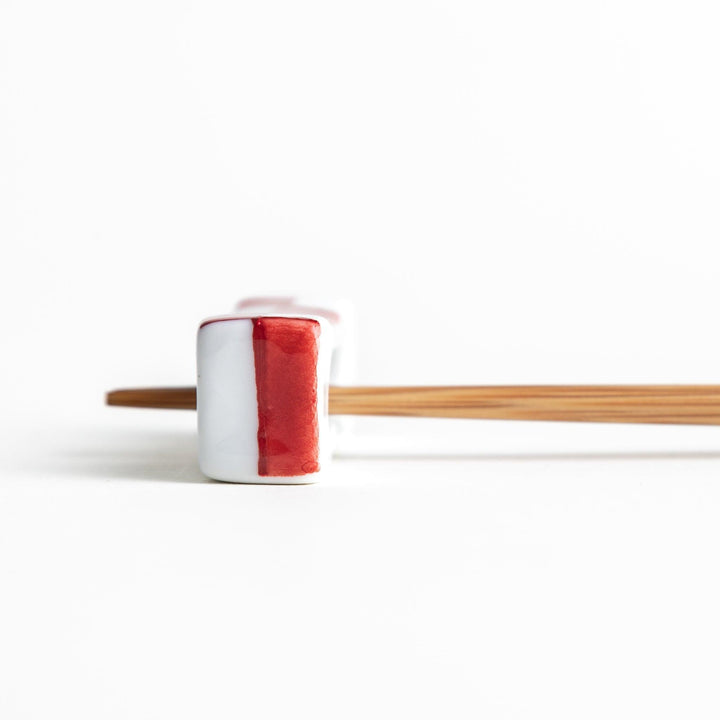 A small rectangular chopsticks rest, white with blue or red stripes arranged in a checkered pattern.