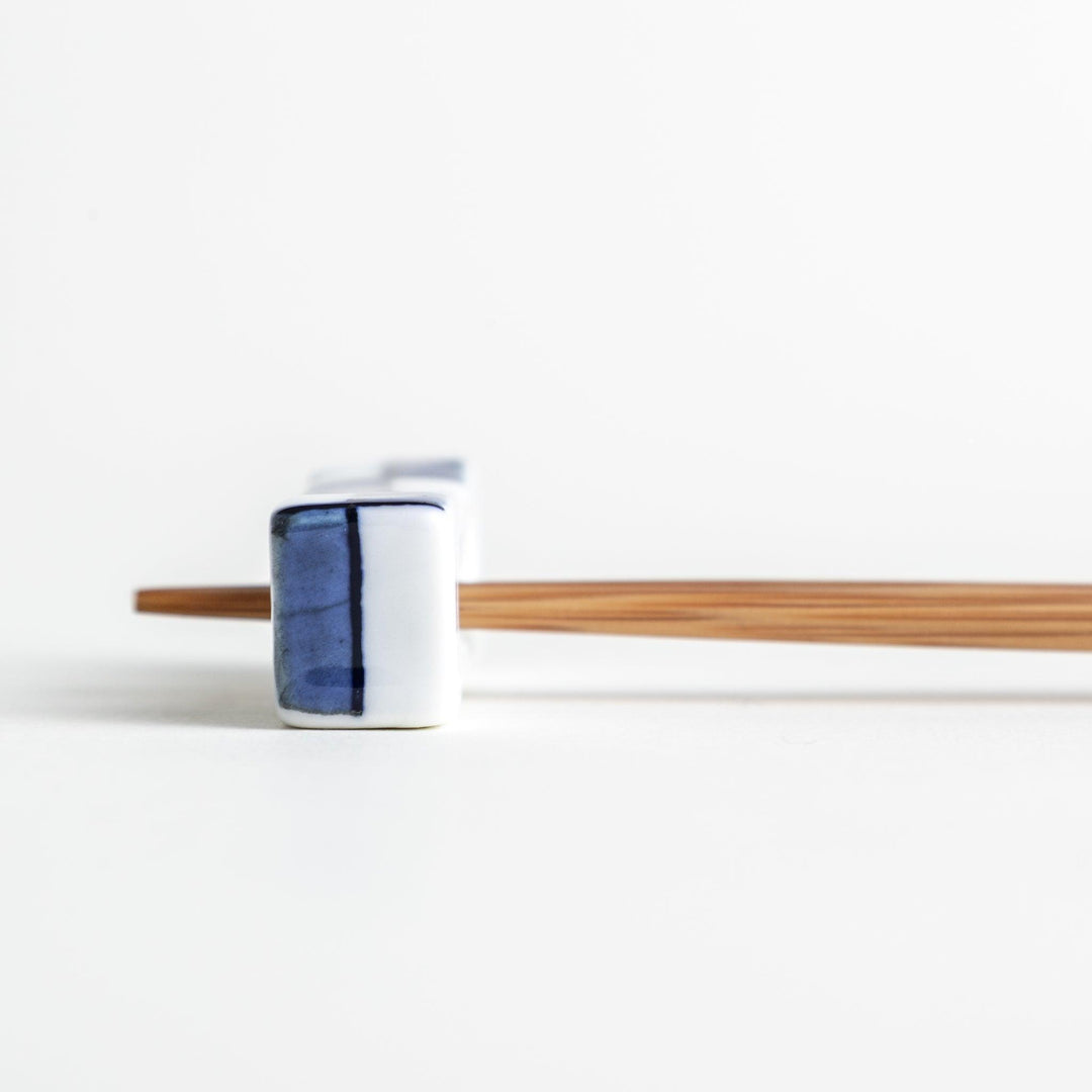 A small rectangular chopsticks rest, white with blue or red stripes arranged in a checkered pattern.