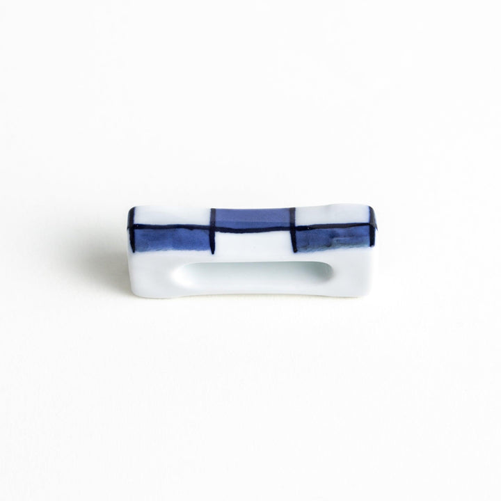 A small rectangular chopsticks rest, white with blue or red stripes arranged in a checkered pattern.