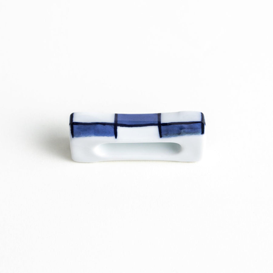 A small rectangular chopsticks rest, white with blue or red stripes arranged in a checkered pattern.