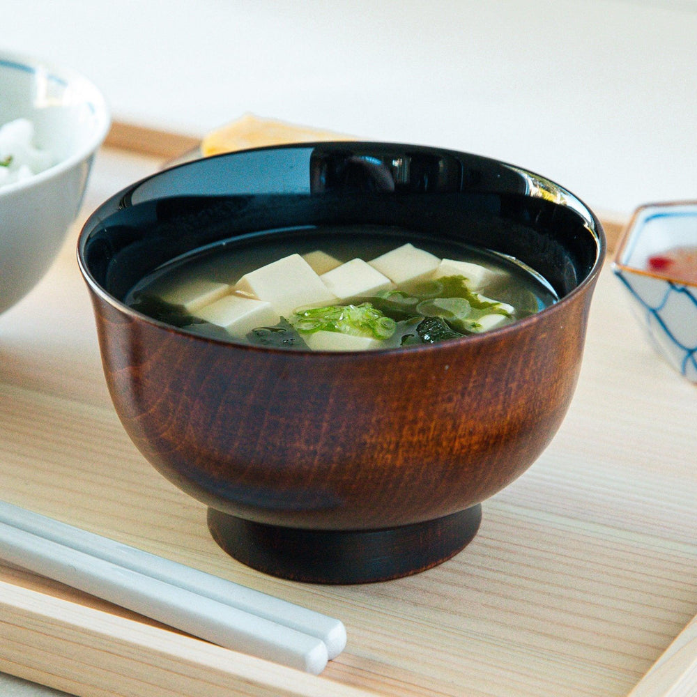 A wooden soup bowl featuring a dark brown grain finish with a sleek black interior.