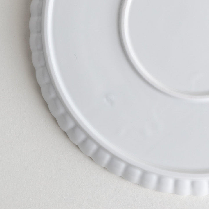 A white ceramic salad plate with a scalloped design with raised edges.