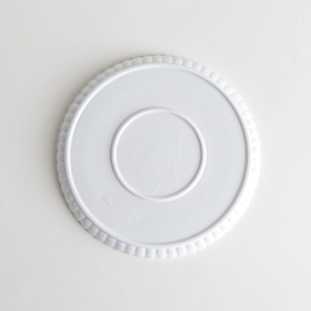 A white ceramic salad plate with a scalloped design with raised edges.