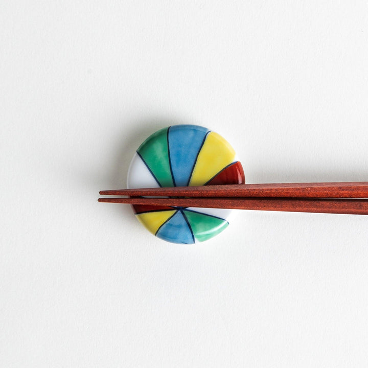 A colorful round ceramic chopstick rest with a pinwheel design.