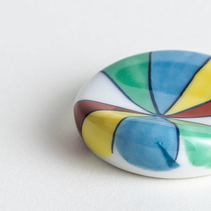 A colorful round ceramic chopstick rest with a pinwheel design.