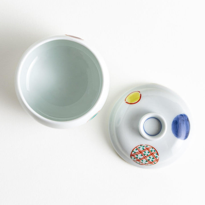 A small, shallow porcelain dish adorned with bold red and blue geometric patterns. The vibrant colors and symmetrical design create a striking contrast against the white background. This dish is perfect for serving condiments or small side dishes, reflecting the clean and precise aesthetics of Japanese tableware.