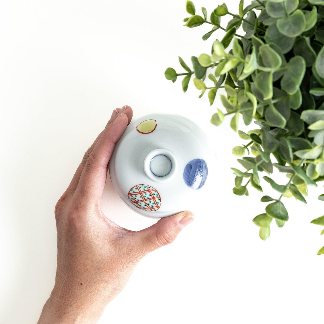 A small, shallow porcelain dish adorned with bold red and blue geometric patterns. The vibrant colors and symmetrical design create a striking contrast against the white background. This dish is perfect for serving condiments or small side dishes, reflecting the clean and precise aesthetics of Japanese tableware.