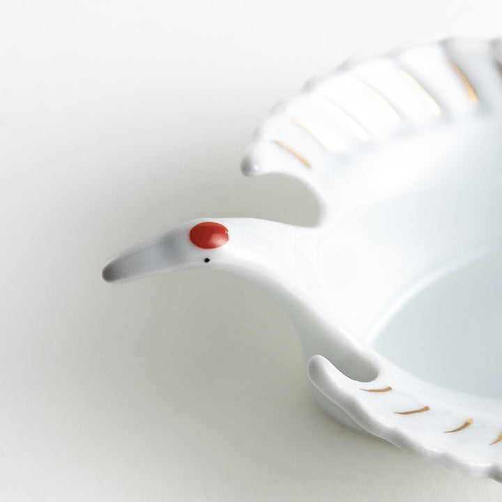 A white, crane-shaped ceramic dish with fine detailing and a small red accent.