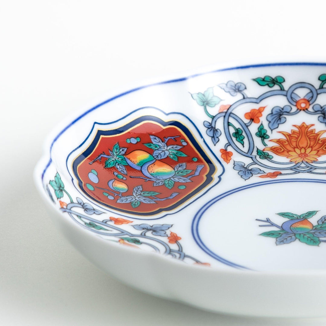 A round dessert plate featuring a central floral design with red, green, and gold patterns, bordered by sections of intricate red and green designs on the scalloped edge.