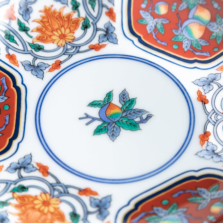 A round dessert plate featuring a central floral design with red, green, and gold patterns, bordered by sections of intricate red and green designs on the scalloped edge.