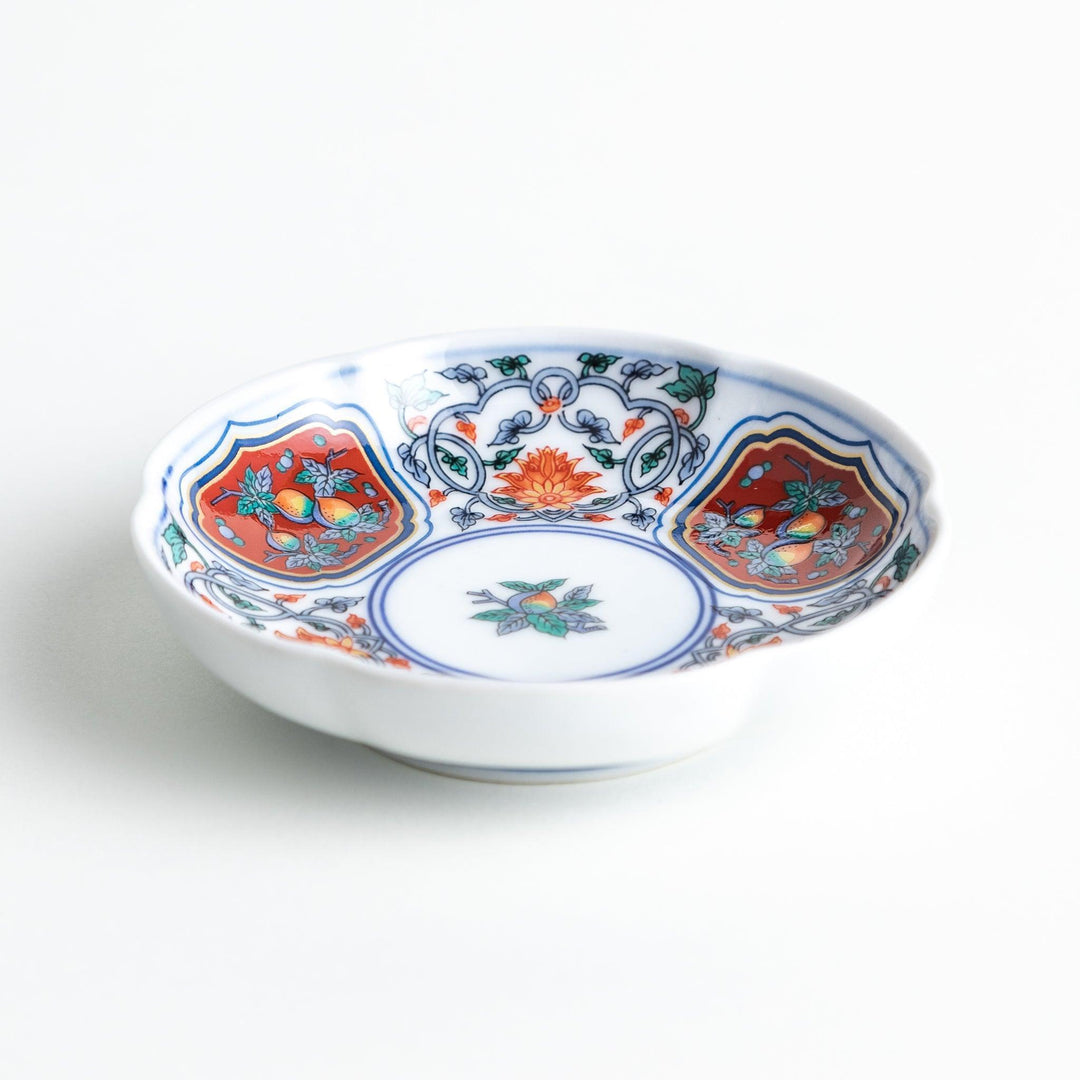 A round sauce dish with a central floral motif, surrounded by red and green floral patterns on the rim with blue accents.