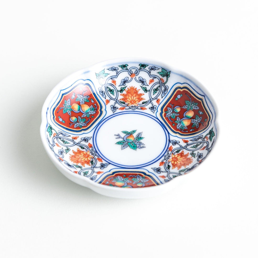 A round sauce dish with a central floral motif, surrounded by red and green floral patterns on the rim with blue accents.