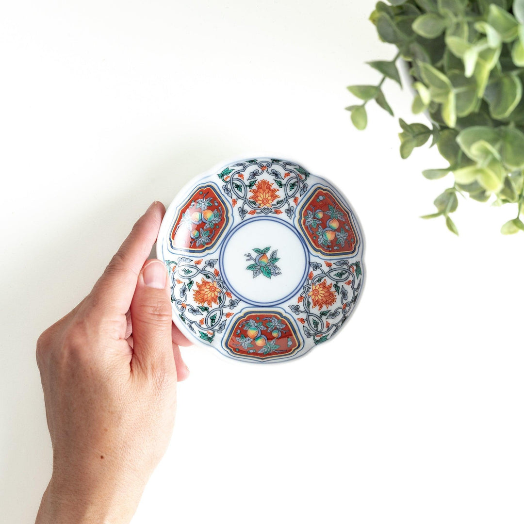 A round sauce dish with a central floral motif, surrounded by red and green floral patterns on the rim with blue accents.