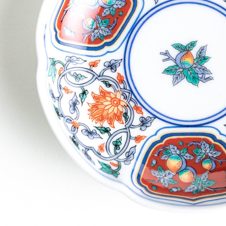 A round sauce dish with a central floral motif, surrounded by red and green floral patterns on the rim with blue accents.