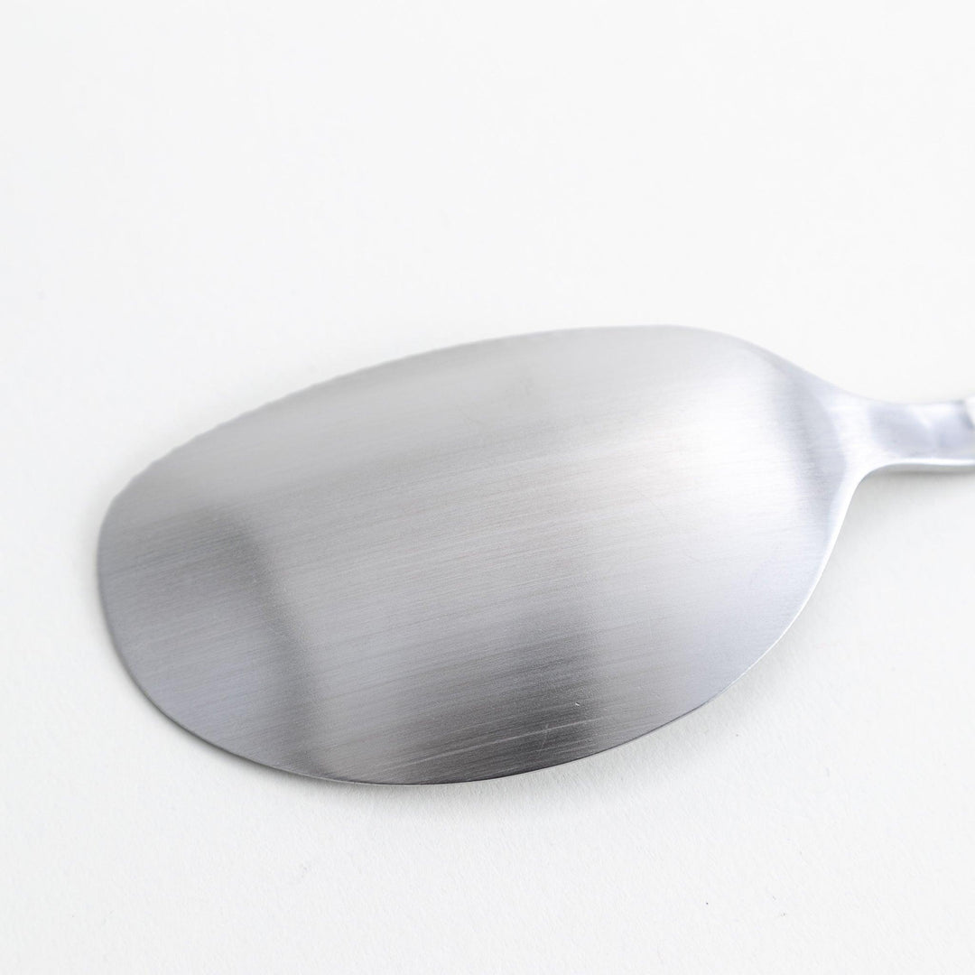 A stainless steel serving spoon with a smooth, polished finish and a slight serrated edge, ideal for cutting and serving.