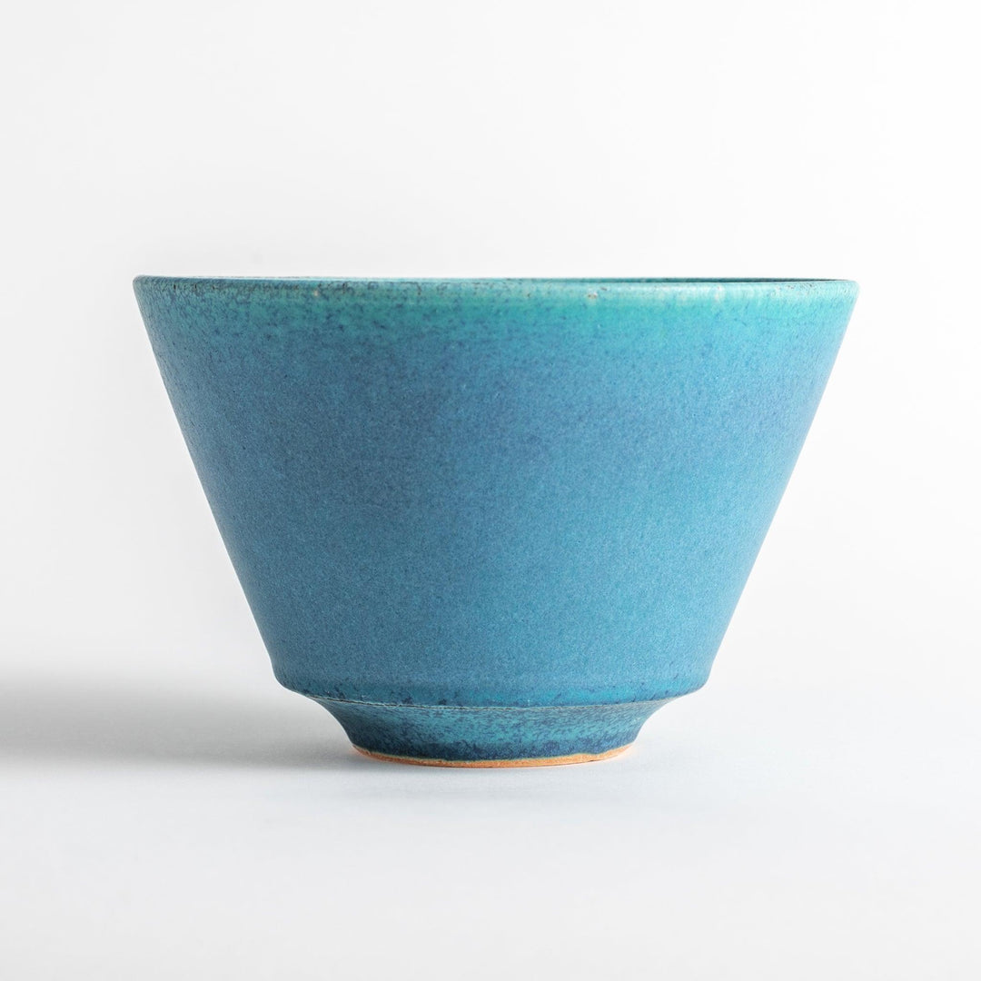 A bowl with a matte turquoise glaze, featuring a minimalist design.