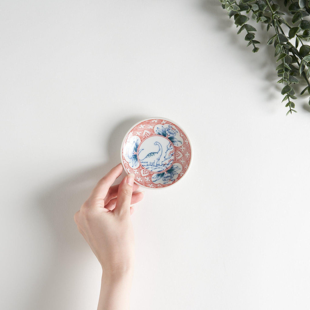 A set of four small, decorative porcelain plates in a gift box, each plate featuring a different dinosaur design in blue and red.