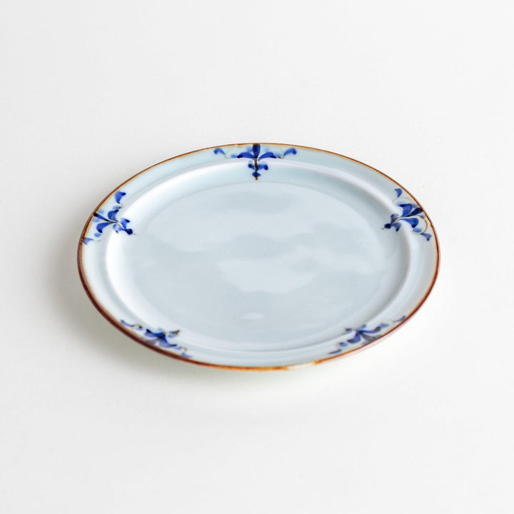 A small porcelain dessert plate with a scalloped edge, decorated with blue and white floral motifs and brown accent trim.