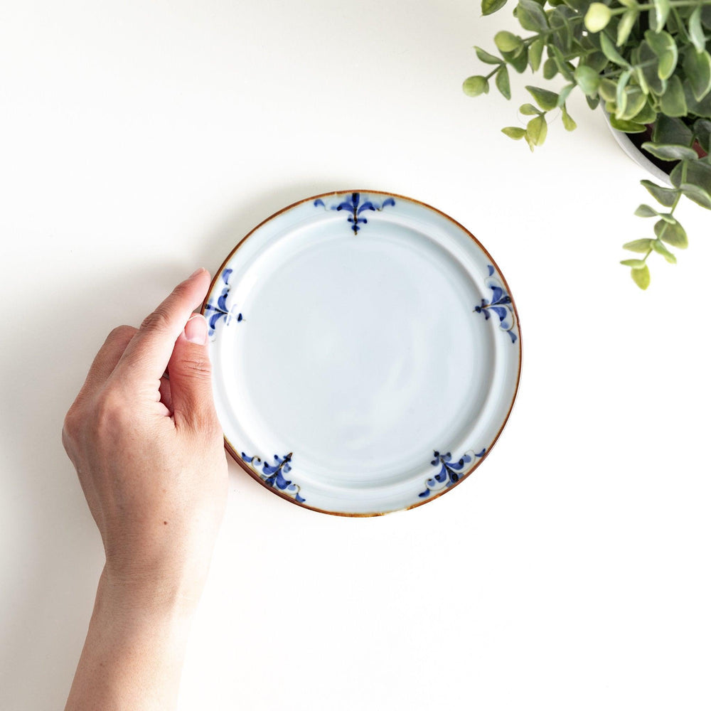 A small porcelain dessert plate with a scalloped edge, decorated with blue and white floral motifs and brown accent trim.