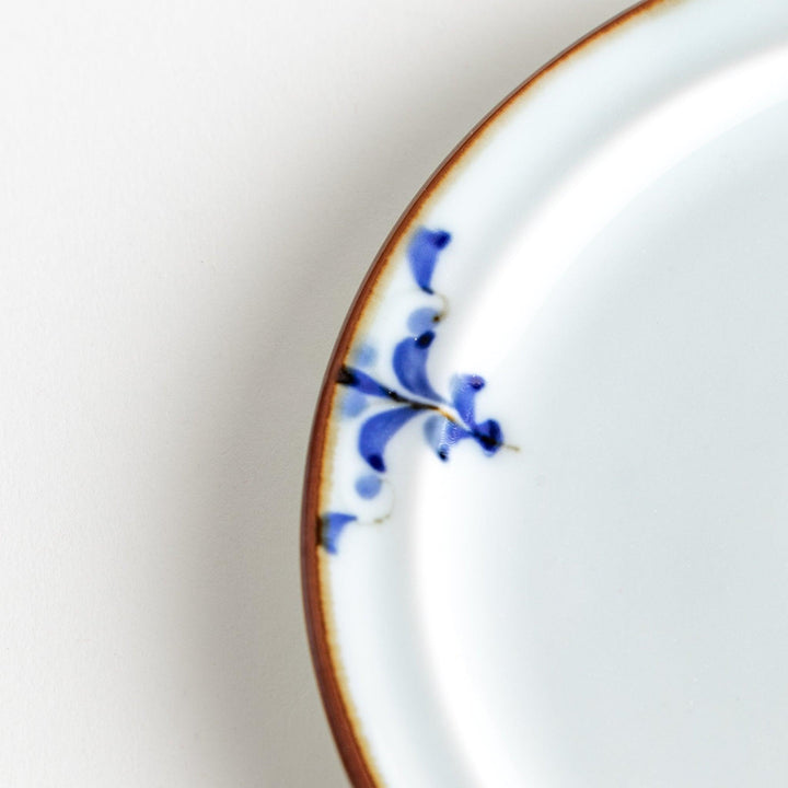 A small porcelain dessert plate with a scalloped edge, decorated with blue and white floral motifs and brown accent trim.