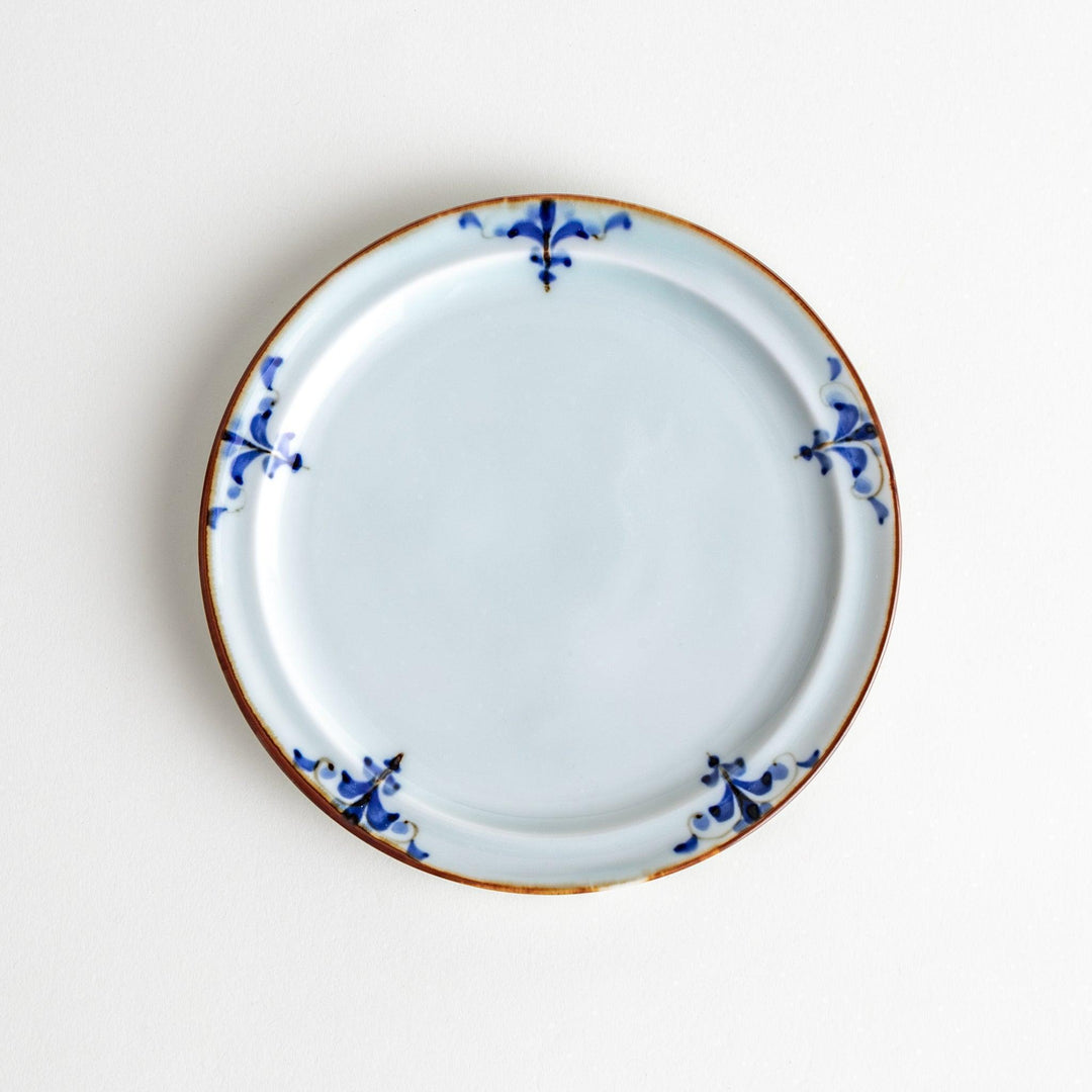 A small porcelain dessert plate with a scalloped edge, decorated with blue and white floral motifs and brown accent trim.