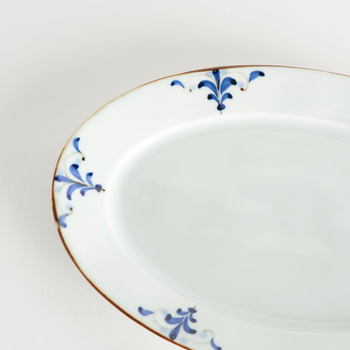 A porcelain oval dinner plate, decorated with blue and white floral motifs with brown accent trim.