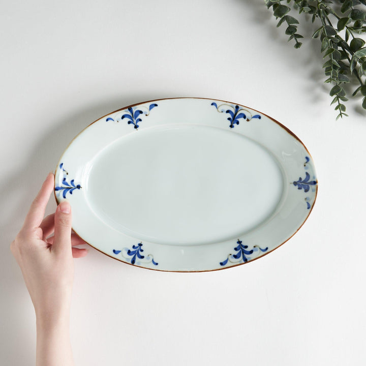 A porcelain oval dinner plate, decorated with blue and white floral motifs with brown accent trim.