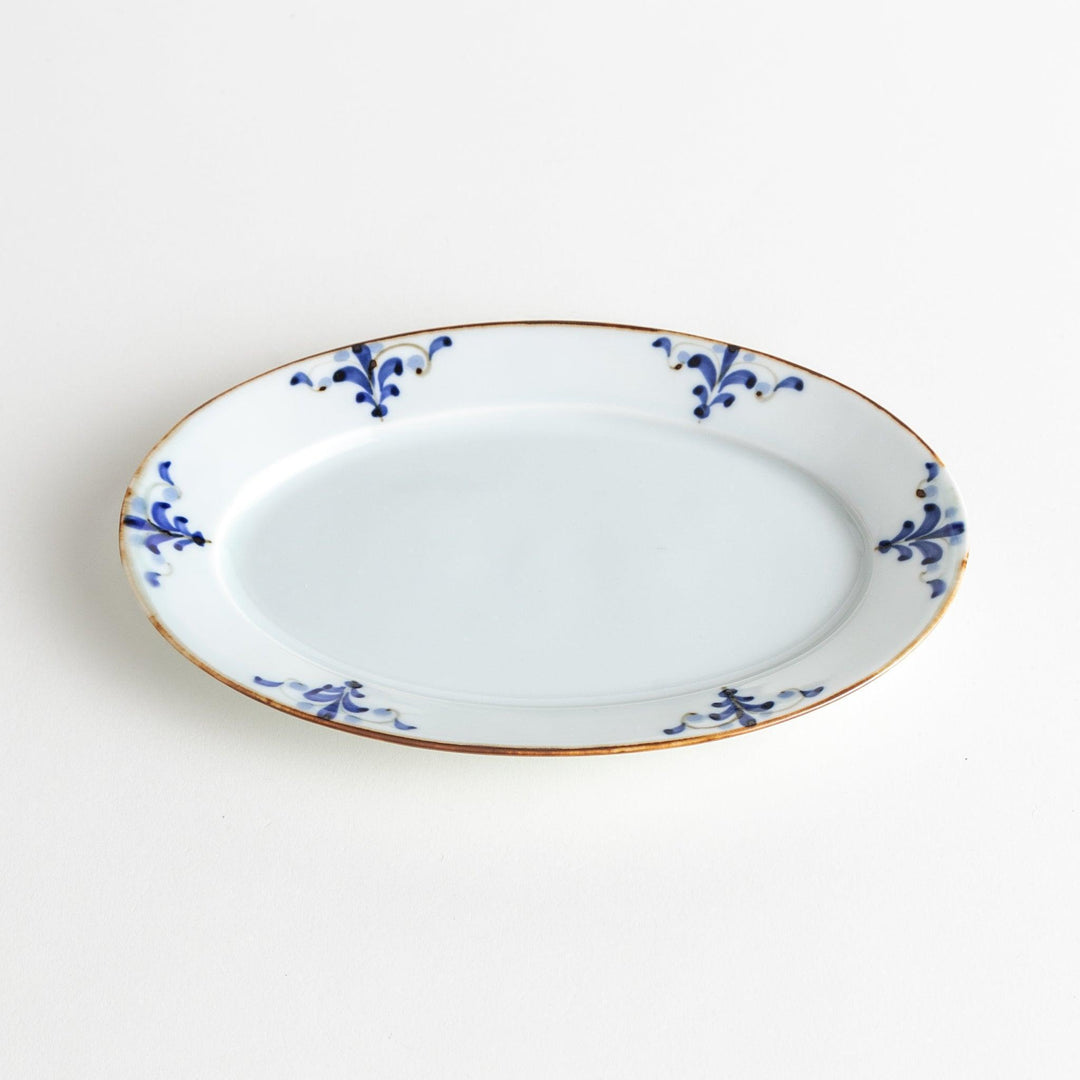 A porcelain oval salad plate, decorated with blue and white floral motifs and brown accent trim.