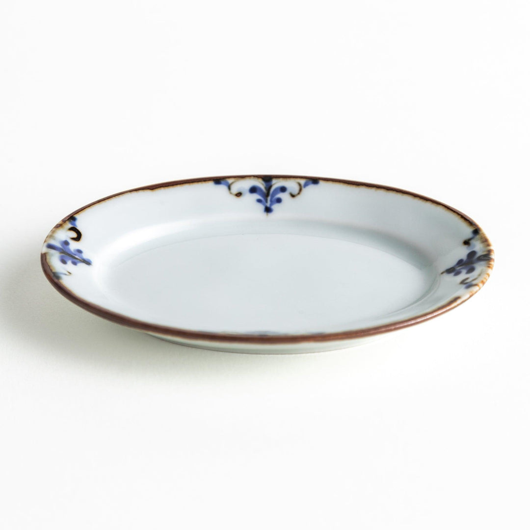 A small porcelain oval sauce dish, decorated with blue and white floral motifs and brown accent trim.