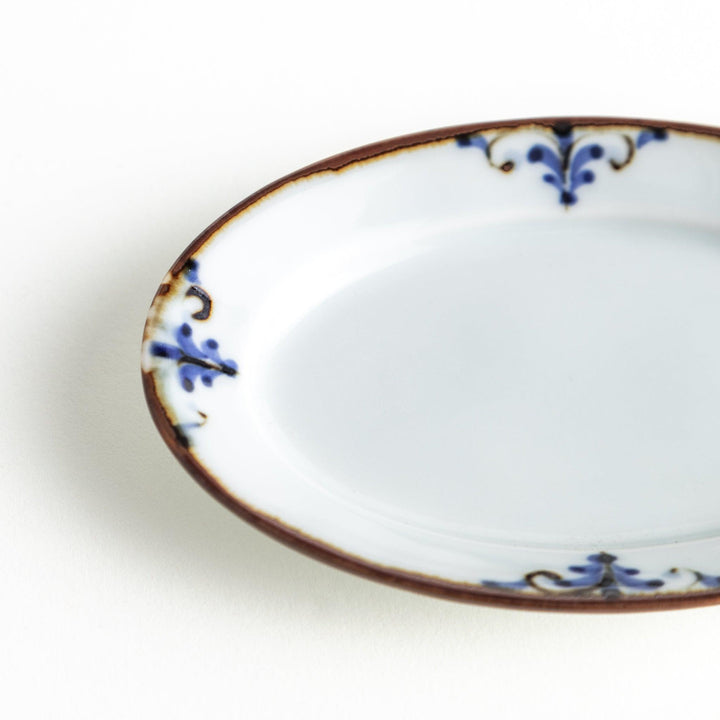 A small porcelain oval sauce dish, decorated with blue and white floral motifs and brown accent trim.