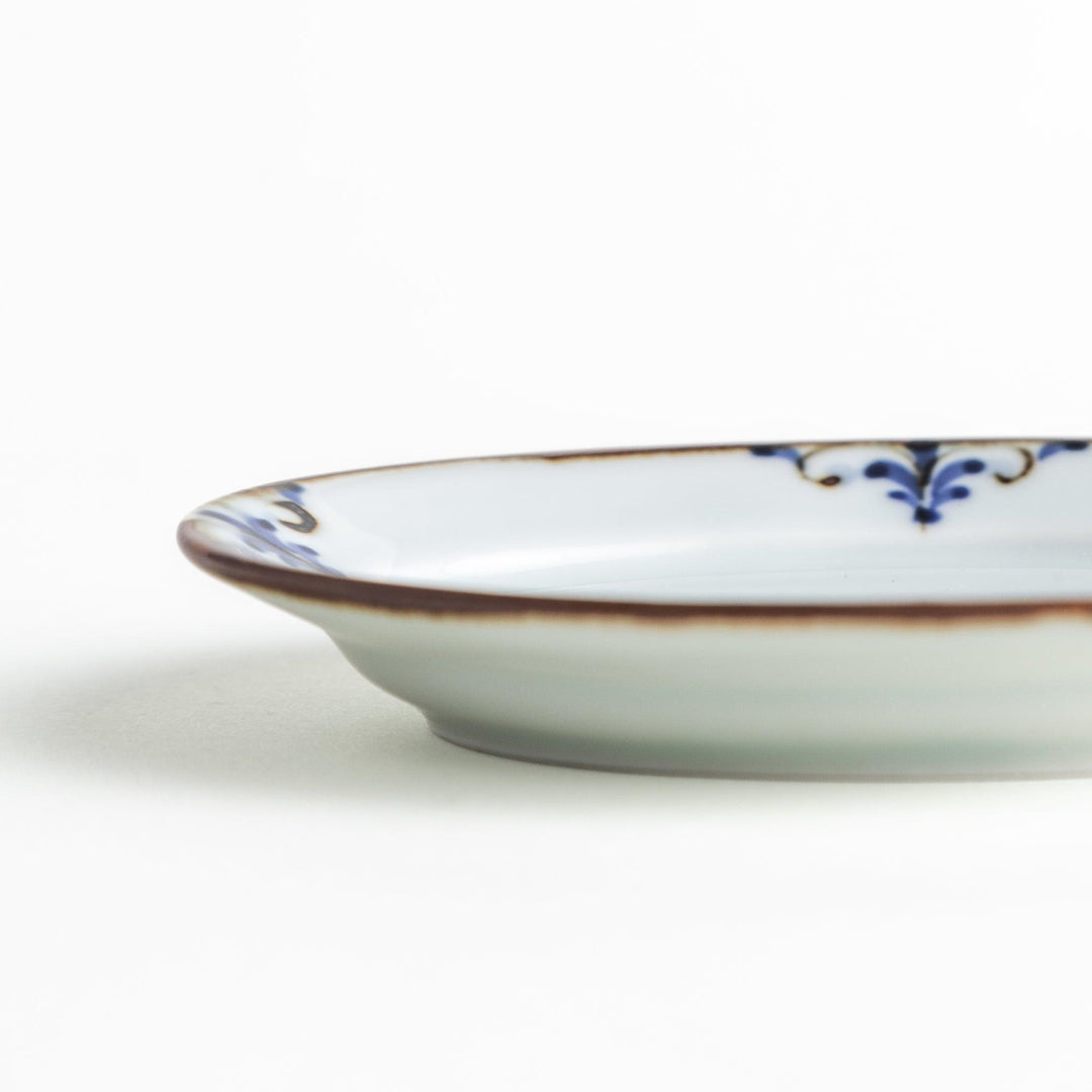 A small porcelain oval sauce dish, decorated with blue and white floral motifs and brown accent trim.