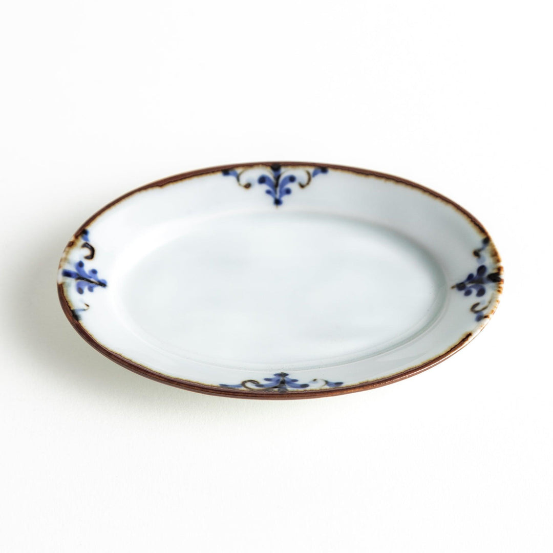 A small porcelain oval sauce dish, decorated with blue and white floral motifs and brown accent trim.