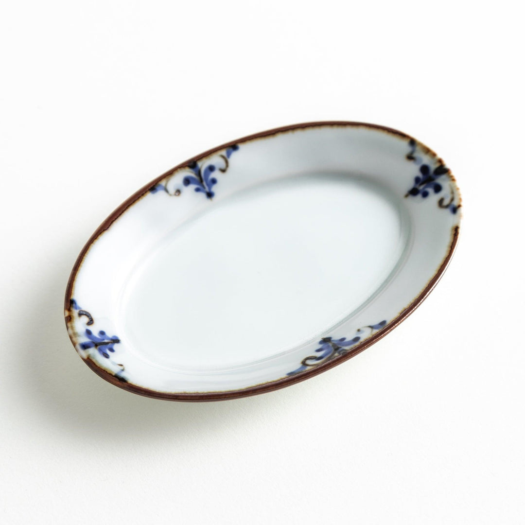 A small porcelain oval sauce dish, decorated with blue and white floral motifs and brown accent trim.