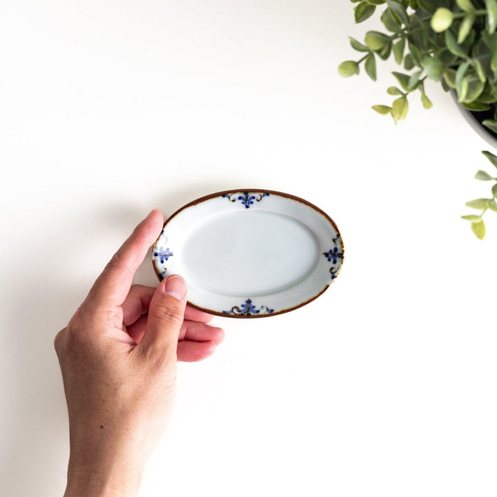 A small porcelain oval sauce dish, decorated with blue and white floral motifs and brown accent trim.